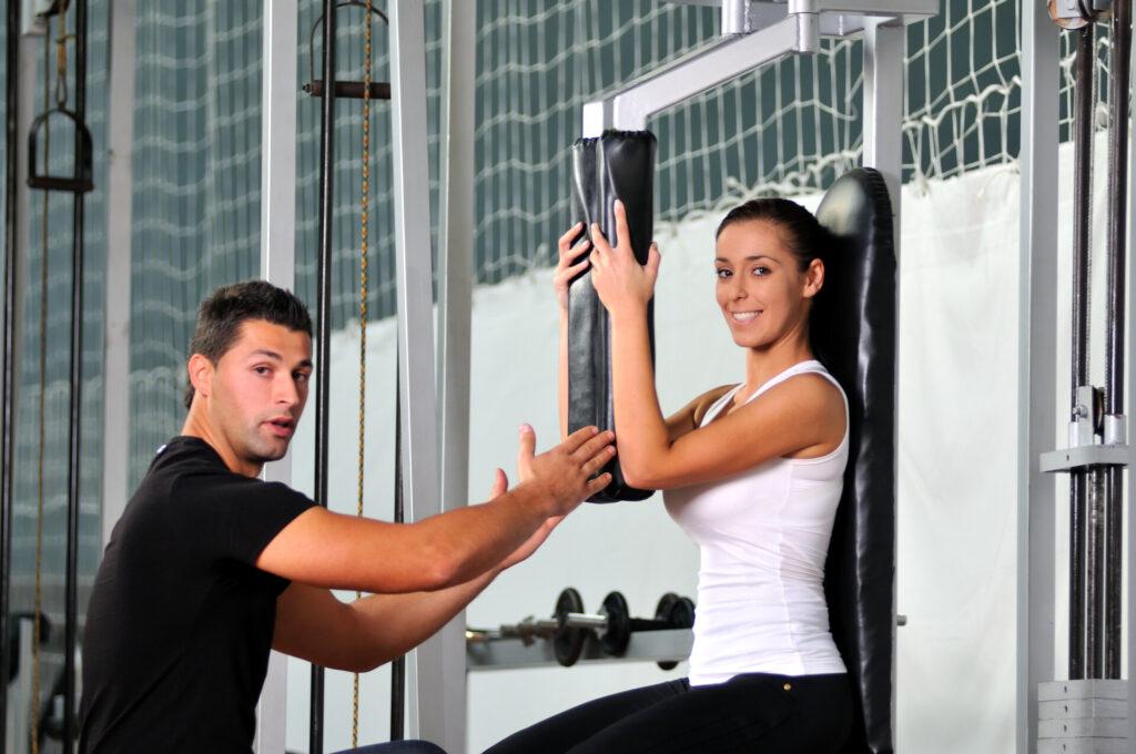 Junge Frau mit ihrem Trainer an der butterfly-Maschine