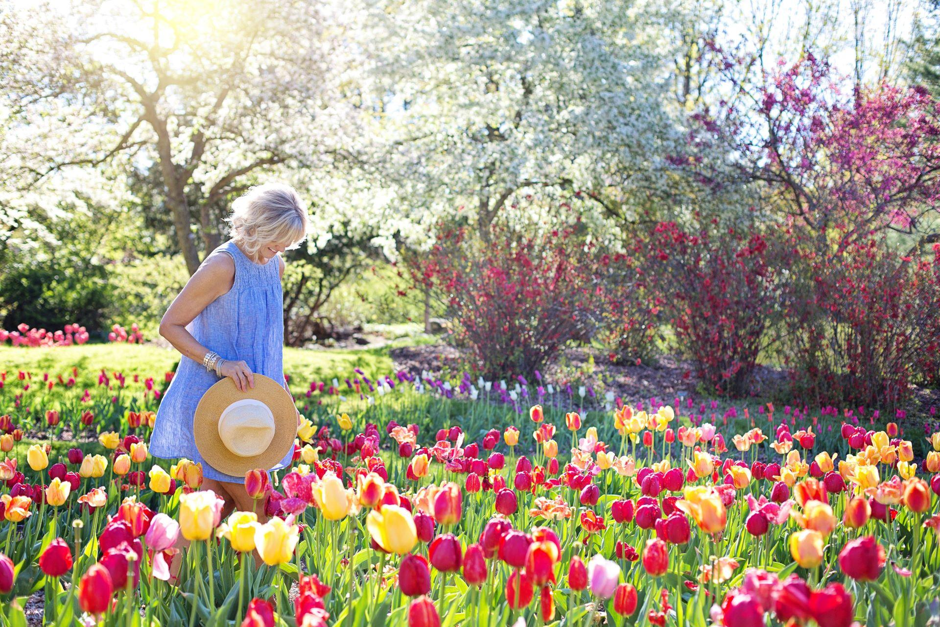 Frau spaziert mit Hut in einem Garten voller Blumen