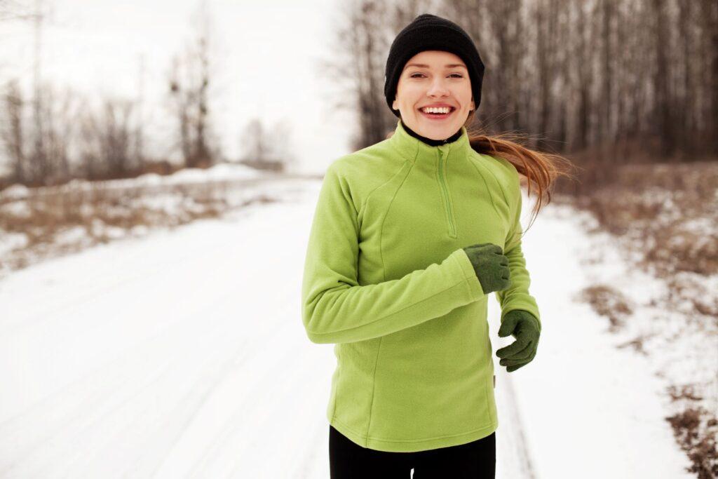 Joggerin in grünem Pullover joggt auf schneebedecktem Weg.
