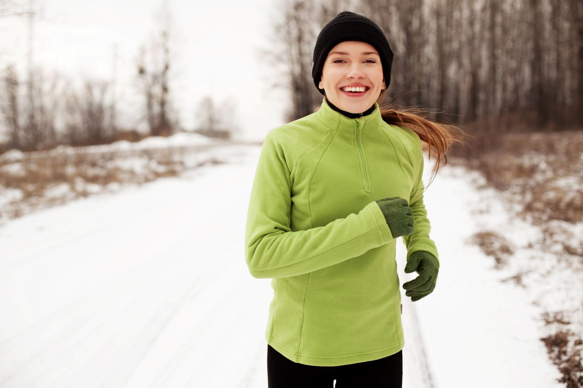 Joggerin in grünem Pullover joggt auf schneebedecktem Weg.