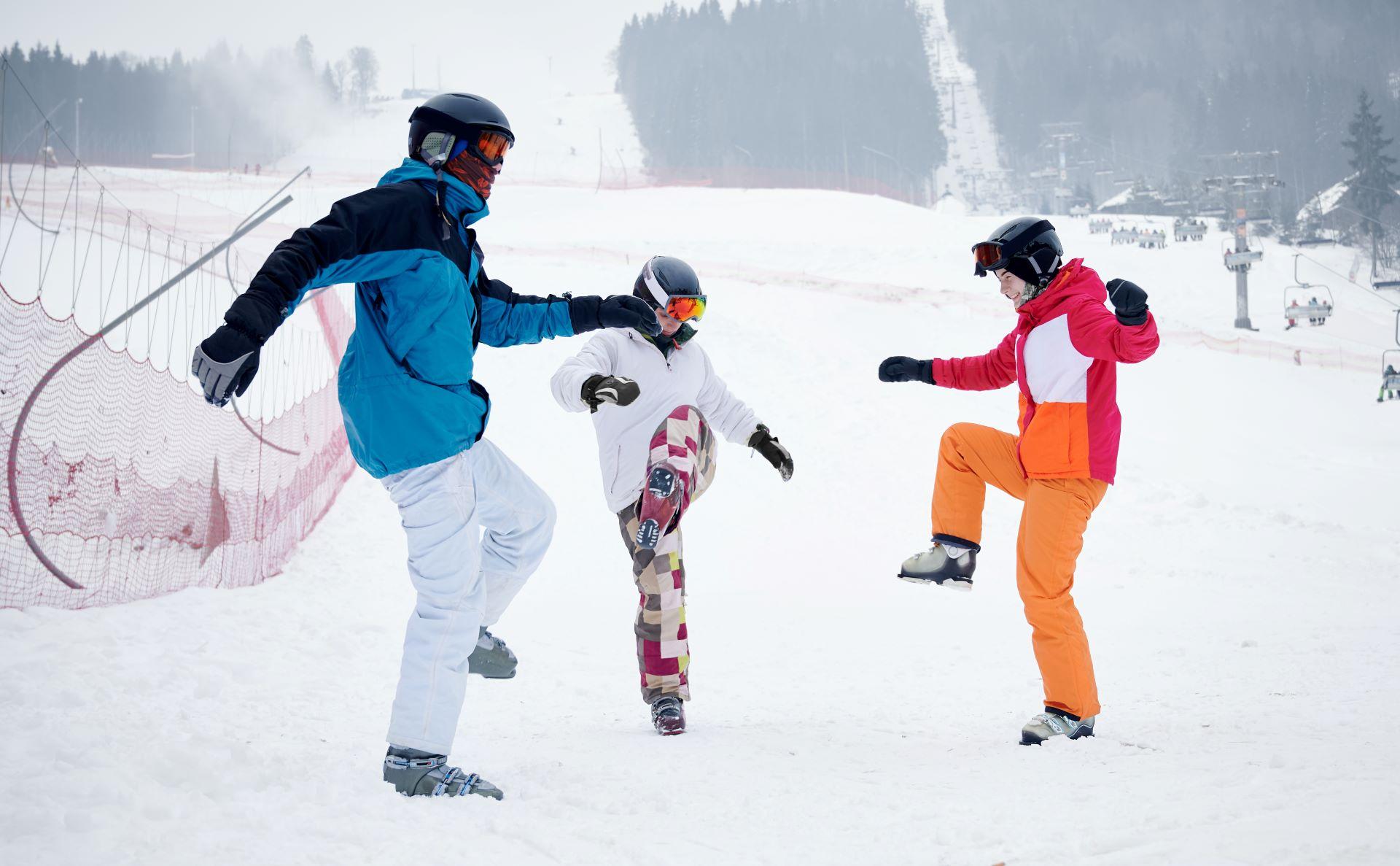 Drei Skifahrer machen Dehnübungen auf der Piste.