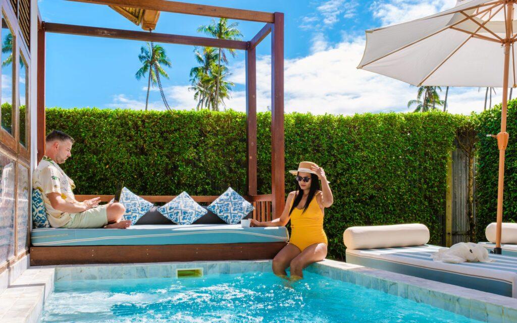 Paar entspannt am Pool mit Daybed und Sonnenschirm unter Palmen