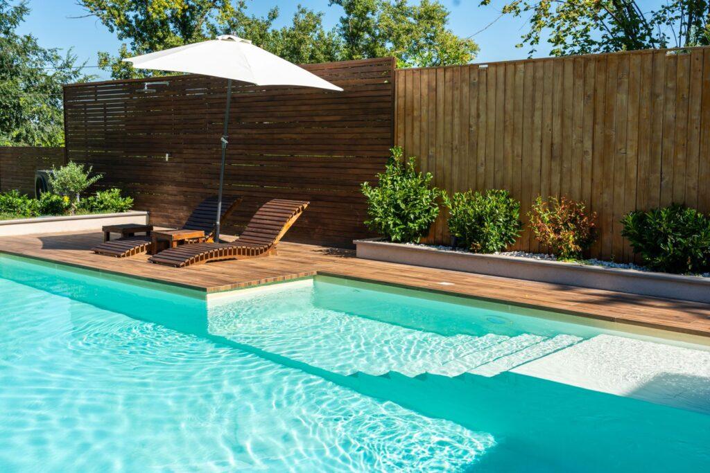 Holzliegestühle auf Pooldeck mit Sonnenschirm und Sichtschutz aus Holz