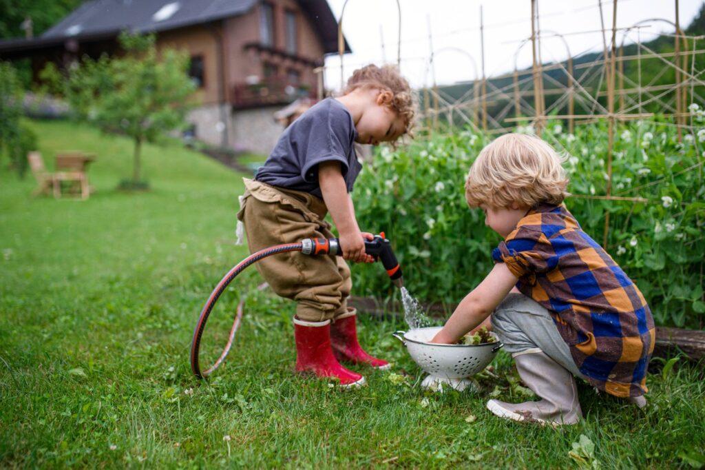 Kinder spielen im Garten mit Wasser und lernen durch Naturerfahrung